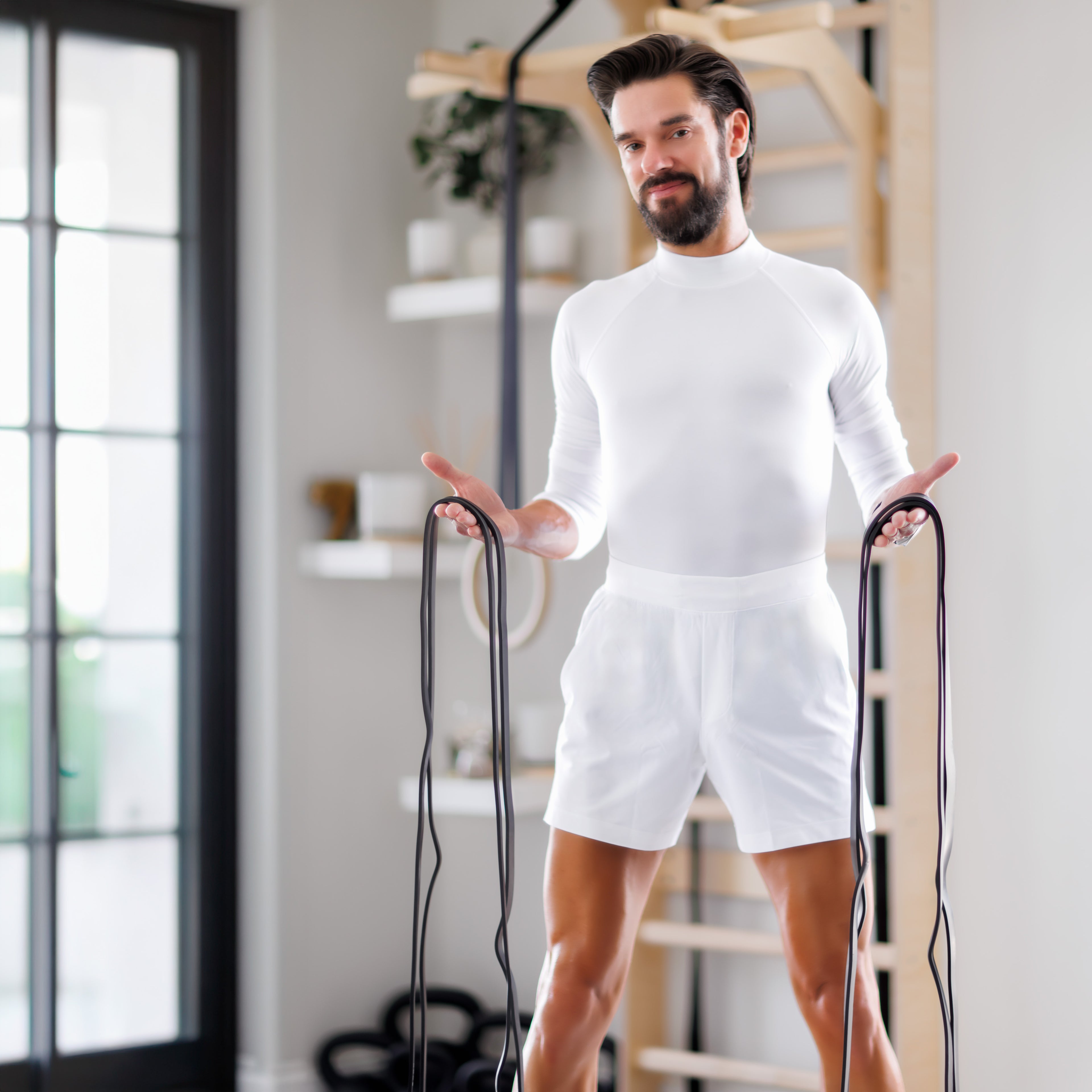 
Personal Practice founder Travis Harris welcomes visitors while holding resistance bands in a bright home studio.